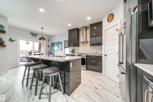 Modern kitchen featuring an island with seating, a stainless steel refrigerator, dark cabinetry, and a light-toned patterned floor - 3514 49 Avenue, Beaumont, AB - Indoor Photo Showing Kitchen With Upgraded Kitchen