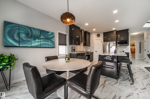 Open concept kitchen and dining area featuring a modern light fixture, recessed lighting, sleek dark cabinetry, and white marble-style floor tiles - 3514 49 Avenue, Beaumont, AB - Indoor Photo Showing Dining Room