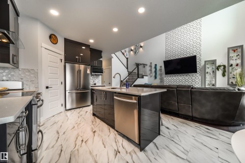 The property features a kitchen with dark cabinetry, stainless steel appliances, and a central island with a sink and dishwasher - 3514 49 Avenue, Beaumont, AB - Indoor Photo Showing Kitchen With Upgraded Kitchen