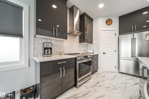 The kitchen features dark grey, high-gloss cabinetry, a white countertop, and a patterned tile backsplash - 3514 49 Avenue, Beaumont, AB - Indoor Photo Showing Kitchen With Upgraded Kitchen