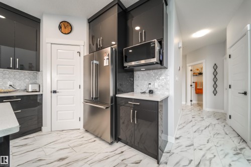 The kitchen features glossy dark cabinetry, a stainless steel refrigerator, and a built-in microwave - 3514 49 Avenue, Beaumont, AB - Indoor Photo Showing Kitchen
