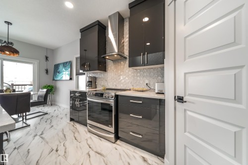The kitchen features dark cabinetry, stainless steel appliances, and a tiled backsplash - 3514 49 Avenue, Beaumont, AB - Indoor Photo Showing Kitchen With Upgraded Kitchen