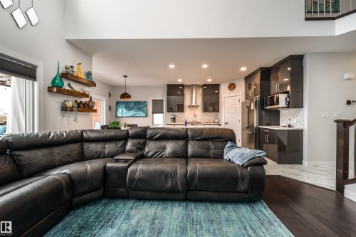 The open concept living area features dark wood flooring, a spacious seating area, and a kitchen with dark cabinetry, stainless steel appliances, and a white tile backsplash - 3514 49 Avenue, Beaumont, AB - Indoor Photo Showing Living Room
