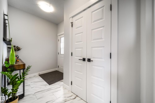 The entry features light-colored walls, white paneled doors with dark hardware, and a white and grey patterned tile floor - 3514 49 Avenue, Beaumont, AB - Indoor Photo Showing Other Room