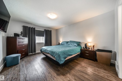 This bedroom features dark wood-style flooring, a window with dark curtains and a blind, and light-colored walls - 3514 49 Avenue, Beaumont, AB - Indoor Photo Showing Bedroom