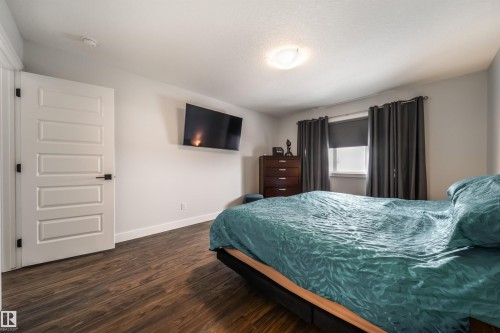 This room features dark wood flooring, a window with dark curtains, and a white interior door with black hardware - 3514 49 Avenue, Beaumont, AB - Indoor Photo Showing Bedroom