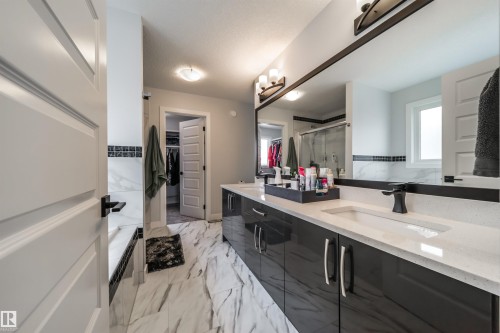 Spacious bathroom featuring a large double vanity with modern dark cabinetry and light countertops, a wide mirror, and marble-style flooring - 3514 49 Avenue, Beaumont, AB - Indoor Photo Showing Bathroom