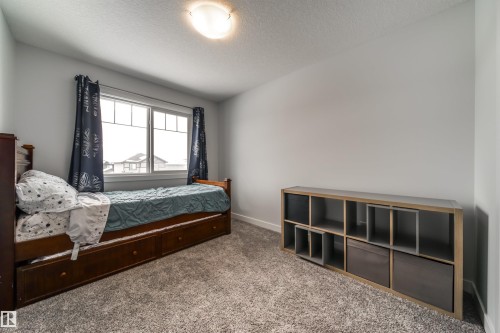 This room features light gray walls, a window with white frames and dark blue curtains, and gray carpeted flooring - 3514 49 Avenue, Beaumont, AB - Indoor Photo Showing Bedroom