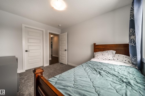 This room features light gray walls, a textured gray carpet, and white interior doors with black hardware - 3514 49 Avenue, Beaumont, AB - Indoor Photo Showing Bedroom