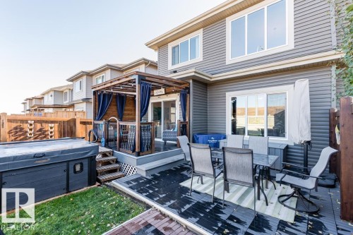 The property features a spacious deck with a dining area, a hot tub, and a pergola with privacy curtains - 3514 49 Avenue, Beaumont, AB - Outdoor