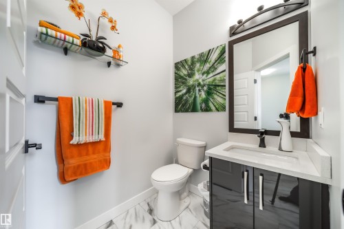 This powder room features a modern vanity with a rectangular sink, a toilet, and white marble-look flooring - 3514 49 Avenue, Beaumont, AB - Indoor Photo Showing Bathroom
