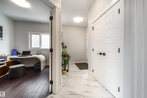 Hallway with white paneled doors, black hardware, and a marble-patterned floor - 3514 49 Avenue, Beaumont, AB - Indoor