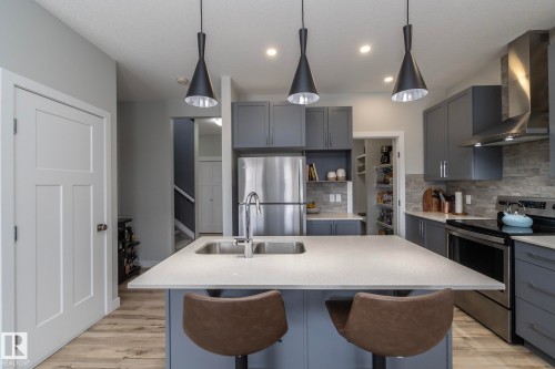 The kitchen features a spacious island with a stainless steel sink, modern pendant lighting, and grey cabinetry - 20650 94A Avenue, Edmonton, AB - Indoor Photo Showing Kitchen With Double Sink With Upgraded Kitchen