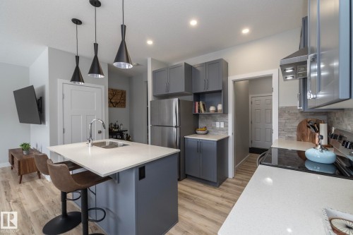 The kitchen features gray cabinetry, light-colored countertops, stainless steel appliances, and a stacked stone backsplash - 20650 94A Avenue, Edmonton, AB - Indoor Photo Showing Kitchen With Double Sink With Upgraded Kitchen