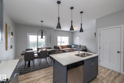 Open concept living area featuring a kitchen island with a double sink, a dining area with a modern chandelier, and light wood-look flooring - 20650 94A Avenue, Edmonton, AB - Indoor Photo Showing Kitchen With Double Sink With Upgraded Kitchen