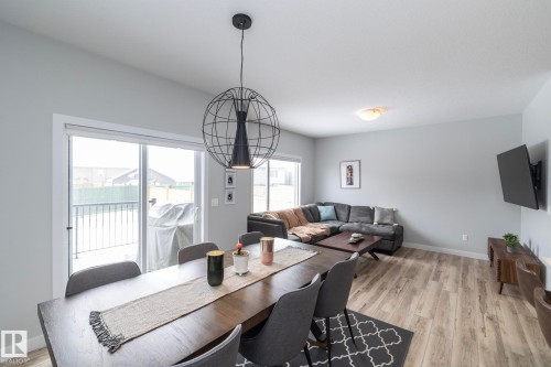 Open concept living area featuring light-colored flooring, a dark wood dining table, and a sliding glass door leading to the exterior - 20650 94A Avenue, Edmonton, AB - Indoor Photo Showing Dining Room