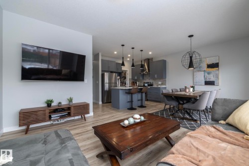 Open concept living space featuring light-toned flooring, a kitchen with grey cabinetry and stainless steel appliances, and a dining area - 20650 94A Avenue, Edmonton, AB - Indoor Photo Showing Living Room