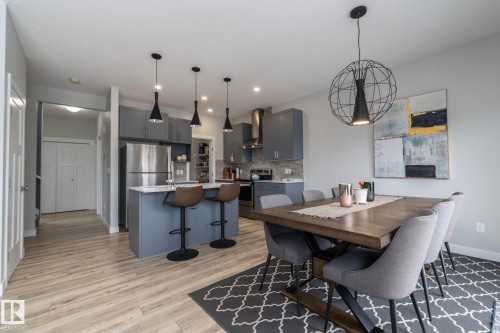 Open-concept living space featuring a dining area with a modern chandelier and a kitchen with an island, pendant lighting, and stainless steel appliances - 20650 94A Avenue, Edmonton, AB - Indoor Photo Showing Dining Room