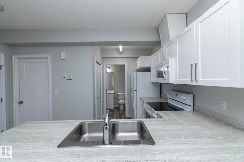 The kitchen features a double basin stainless steel sink, light-colored countertops, white upper and lower cabinetry, and a white oven with a cooktop - 20650 94A Avenue, Edmonton, AB - Indoor Photo Showing Kitchen With Double Sink