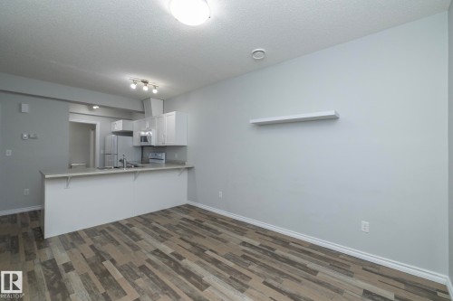 The open concept living area features resilient plank flooring, a contemporary kitchen with white cabinetry, a kitchen island, and stainless steel appliances - 20650 94A Avenue, Edmonton, AB - Indoor Photo Showing Kitchen