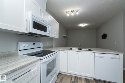 The kitchen features white cabinetry, a double basin sink, and white appliances including a range, microwave, and dishwasher - 20650 94A Avenue, Edmonton, AB - Indoor Photo Showing Kitchen With Double Sink
