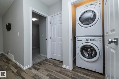 Laundry area featuring a stacked washer and dryer, complemented by wood-look flooring and white trim - 20650 94A Avenue, Edmonton, AB - Indoor Photo Showing Laundry Room