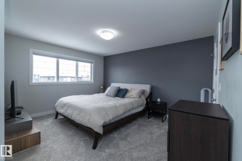 This bedroom features a light grey carpet, a large window with white trim, and a ceiling-mounted light fixture - 20650 94A Avenue, Edmonton, AB - Indoor Photo Showing Bedroom