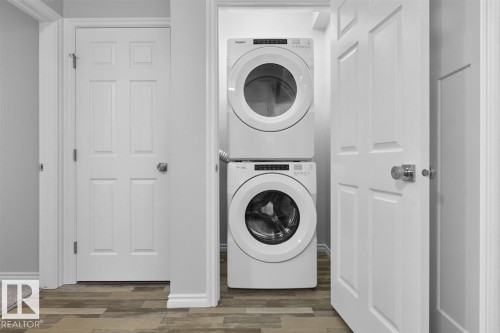 Laundry area featuring a stacked washer and dryer, white paneled doors, and wood-style flooring - 20650 94A Avenue, Edmonton, AB - Indoor Photo Showing Laundry Room