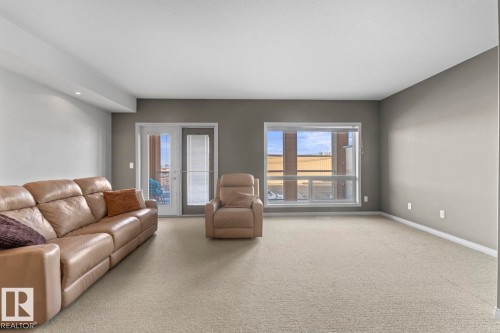 Living area featuring light-colored carpeting, a window providing natural light, and a double glass door leading to an outdoor space - 107 801 11 Street, Cold Lake, AB - Indoor Photo Showing Living Room