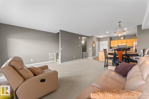 Open concept living area with carpeting, grey walls, and a view into the kitchen featuring wooden cabinetry and a dining area - 107 801 11 Street, Cold Lake, AB - Indoor Photo Showing Living Room