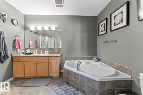 Bathroom featuring a vanity with a single sink, a large mirror, and a corner bathtub with tiled surround - 107 801 11 Street, Cold Lake, AB - Indoor Photo Showing Bathroom