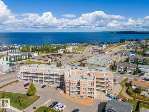 The property features a multi-story building with balconies, surrounded by a paved parking area and landscaped green spaces - 107 801 11 Street, Cold Lake, AB - Outdoor With Body Of Water With View
