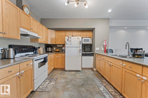 The kitchen features light wood cabinetry, white appliances, and a double basin sink with a chrome faucet - 107 801 11 Street, Cold Lake, AB - Indoor Photo Showing Kitchen With Double Sink