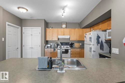 The kitchen features light wood cabinetry, a stainless steel sink with a high arc faucet, and a range with a microwave above it - 107 801 11 Street, Cold Lake, AB - Indoor Photo Showing Kitchen