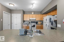 The kitchen features light wood cabinetry, a stainless steel sink with a high arc faucet, and a range with a microwave above it - 