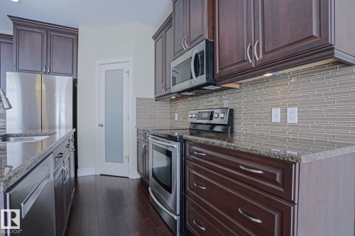 The kitchen features dark wood cabinetry, granite countertops, and stainless steel appliances - 2315 Ashcraft Cape, Edmonton, AB - Indoor Photo Showing Kitchen With Upgraded Kitchen
