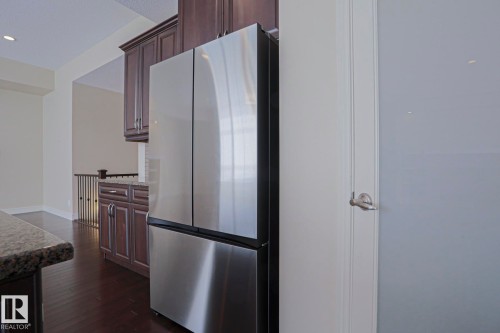 Kitchen featuring dark wood cabinetry, granite countertops, and a stainless steel refrigerator - 2315 Ashcraft Cape, Edmonton, AB - Indoor