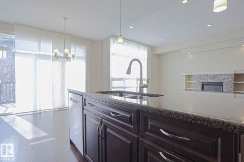 The kitchen island features dark wood cabinetry, a granite countertop, and an undermount sink with a gooseneck faucet - 2315 Ashcraft Cape, Edmonton, AB - Indoor Photo Showing Kitchen With Double Sink