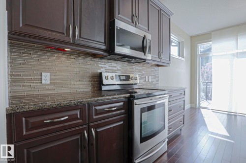 The kitchen features dark wood cabinetry, granite countertops, and a full suite of stainless steel appliances - 2315 Ashcraft Cape, Edmonton, AB - Indoor Photo Showing Kitchen With Upgraded Kitchen