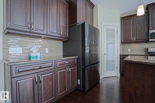 The kitchen features dark wood cabinetry, a tiled backsplash, and dark flooring - 2315 Ashcraft Cape, Edmonton, AB - Indoor Photo Showing Kitchen