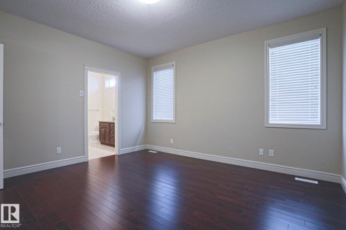 The room features dark wood flooring, light neutral-colored walls, and two windows with white blinds - 2315 Ashcraft Cape, Edmonton, AB - Indoor Photo Showing Other Room