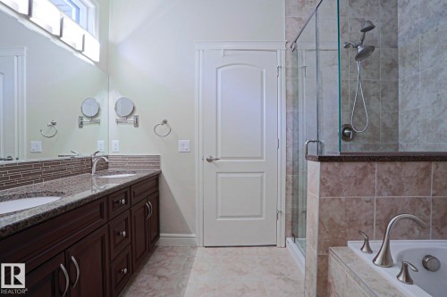 Bathroom featuring dual sinks with granite countertops, dark wood cabinetry, and a glass-enclosed shower - 2315 Ashcraft Cape, Edmonton, AB - Indoor Photo Showing Bathroom