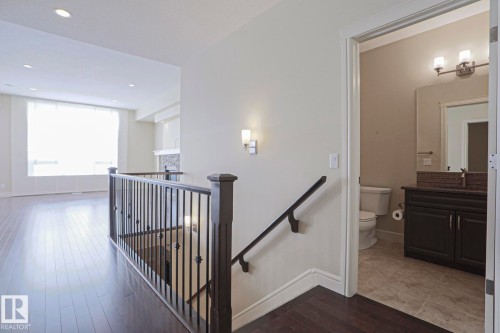This landing features rich hardwood floors, a dark wood and iron banister, and a wall-mounted light fixture - 2315 Ashcraft Cape, Edmonton, AB - Indoor Photo Showing Other Room
