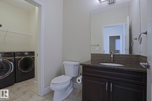 This property features a bathroom with a dark wood vanity, a granite countertop, and a tiled backsplash - 2315 Ashcraft Cape, Edmonton, AB - Indoor Photo Showing Laundry Room