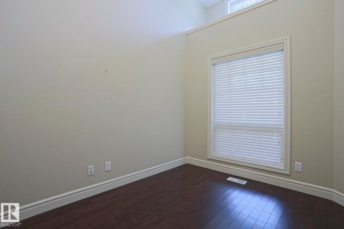 This room features dark hardwood flooring, light-colored walls, and a large window with white blinds - 2315 Ashcraft Cape, Edmonton, AB - Indoor Photo Showing Other Room