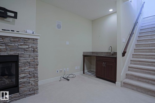 The property features a stone-clad fireplace and a wet bar with a dark wood cabinet, granite countertop, and stainless steel sink - 2315 Ashcraft Cape, Edmonton, AB - Indoor With Fireplace