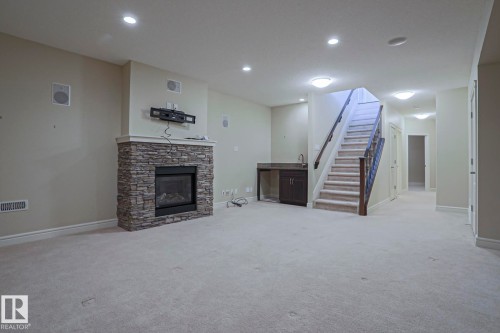 This spacious room features a stone-clad fireplace, light-colored carpeting, recessed lighting, and a built-in wet bar with dark cabinetry and a stone countertop - 2315 Ashcraft Cape, Edmonton, AB - Indoor With Fireplace