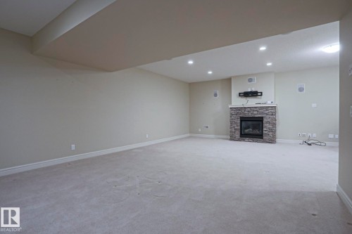 Expansive room with neutral carpeting, a stone-clad fireplace, and recessed lighting - 2315 Ashcraft Cape, Edmonton, AB - Indoor With Fireplace