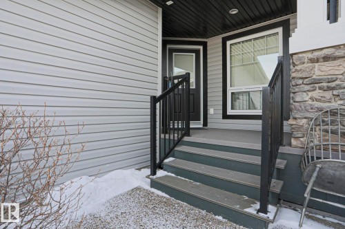 The property features light-colored horizontal siding, a dark front door, and a multi-level deck with dark railings - 2315 Ashcraft Cape, Edmonton, AB - Outdoor With Exterior