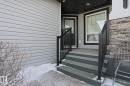 The property features light-colored horizontal siding, a dark front door, and a multi-level deck with dark railings - 2315 Ashcraft Cape, Edmonton, AB  - Outdoor With Exterior 